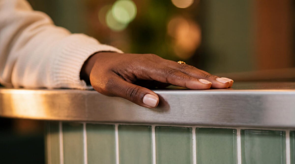 Client's hand with a neat classic manicure and natural nude nails resting on a salon counter