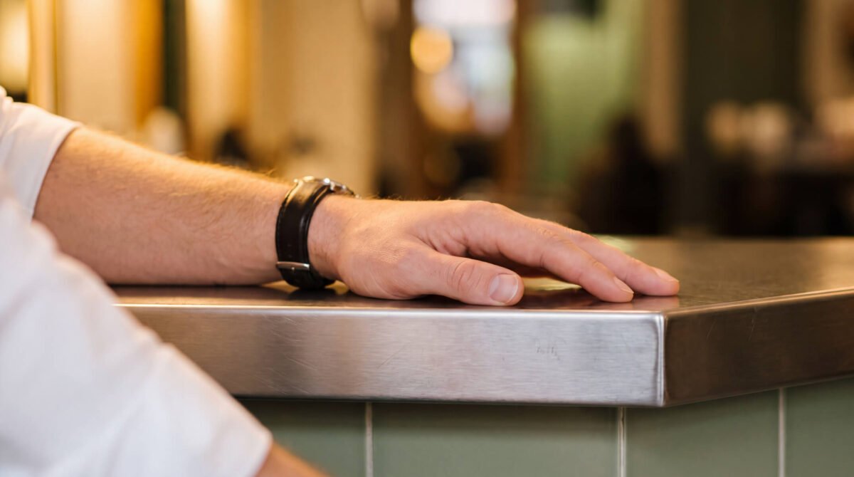 Man's hand with short, buffed nails after a mens manicure, resting on a salon counter