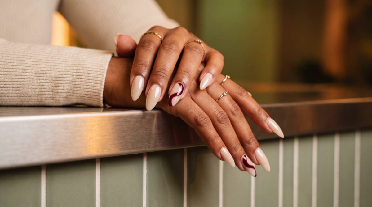 Long almond BIAB nail extensions with a red accent nail on a hand wearing gold rings