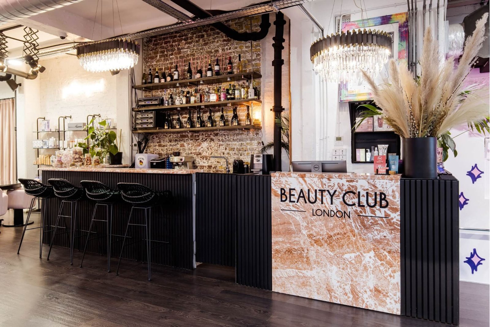 Cocktail bar inside Beauty Club London, with a marble counter, bottle-lined brick wall and black bar stools